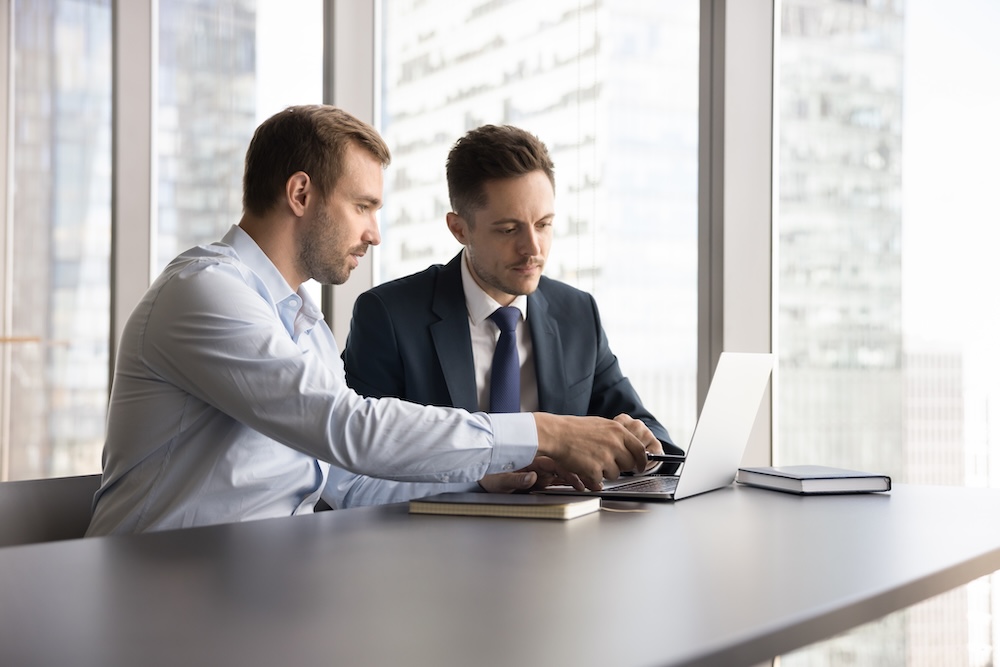 Colleagues working together on joint project or task met in skyscraper office with city view, look at laptop, share ideas, solutions and strategy, planning cooperation, engaged in teamwork.