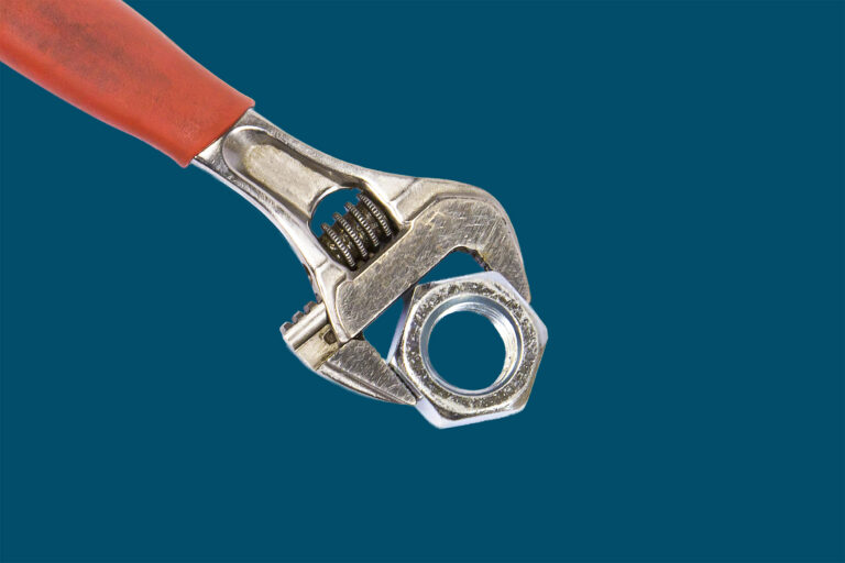 Adjustable wrench tightening a bolt against a solid Navy blue background